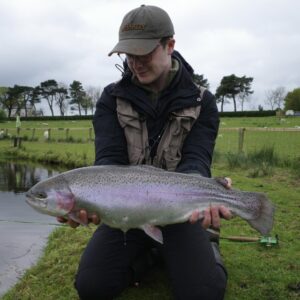 A fly fisherman holds up a large rainbow trout.