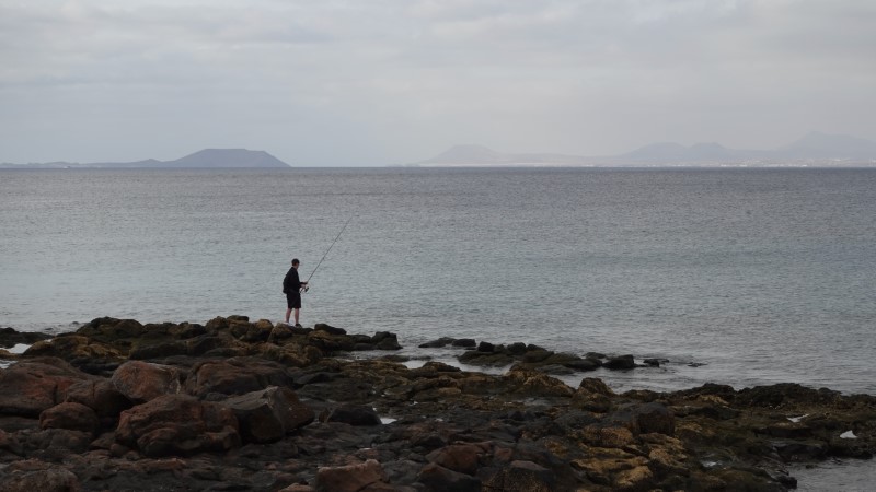 A fisherman fishes from the rocks of a tropical destination. 