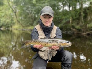 A fly fisherman holds out a brown trout for a photograph. 