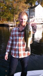 Happy man holds up largemouth bass while standing on a boat deck.