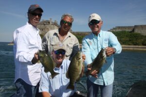 Three men stand on a boat, each holding a bass of their own.