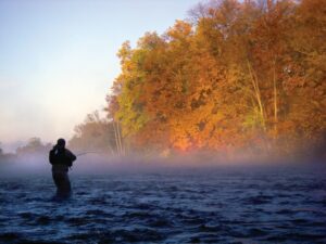 A fisherman stands along a large river fishing.