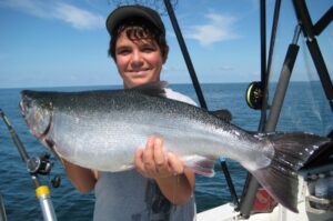 A happy boy holds up a large coho he caught on a boat.