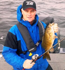 A pro fisherman named Heaney holds out a smallmouth bass.
