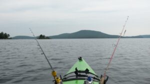 A fishing kayak with two rods attached to it's hull, moving across a large open lake. 