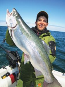 A happy fisherman proudly holds up a large steelhead. 