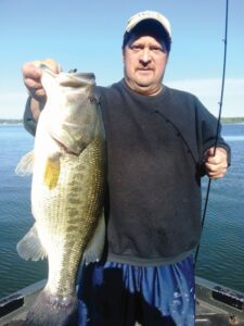 Angler holds his rod and a large bass he caught while fishing.