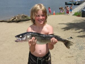 A small child holds out a large walleye.