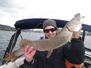 An enthusiastic angler holds up a Northern Pike while out boat fishing. 