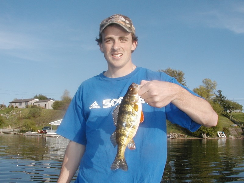  A young man holds a small perch up by its mouth.