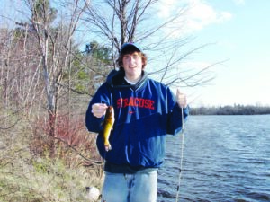 A young angler holds out a brown bullhead he caught while shore fishing from the lake.