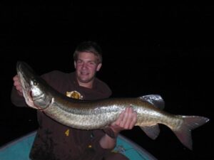 A fisherman named Mike holds up a massive musky he caught while boat fishing. 