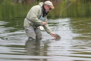 A fly fisherman lips a smallmouth bass while standing in the water.