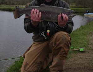A fly fisherman holds out a steelhead. 
