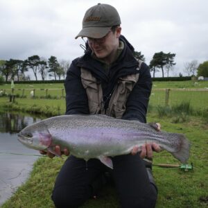 A proud fly fisherman holds up a chunky rainbow trout. 