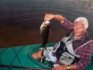 An angler holds up a largemouth bass while canoe fishing.