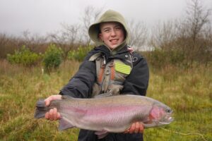 A young angler holds up a big rainbow trout. 