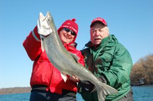 Two anglers pose for a photo with an impressive lake trout they caught on rod and line.