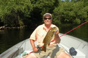 A happy lure fisherman holds up a smallmouth bass he caught while boat fishing with a baitcaster. 