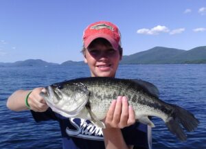 A young angler holds up a large mouth bass while out on a boat. 