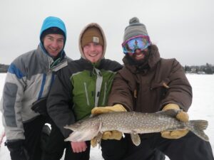 Three fishermen take a photo with a small northern pike. 