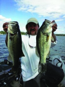 A fisherman holds up two largemouth bass while fishing on an extensive lake. 
