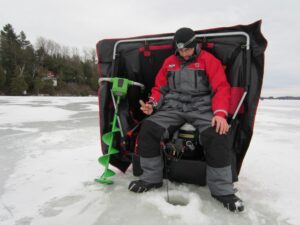 An ice fisherman sits jigging in a hole he made with his auger.