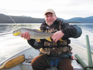 A proud angler showcases a lake trout at the hull of his boat. 