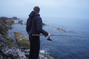 A lure fisherman stands at the coast fishing for striped bass. 