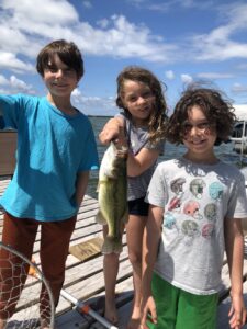 Three happy anglers hold up a largemouth bass while fishing from a dock in New York State. 