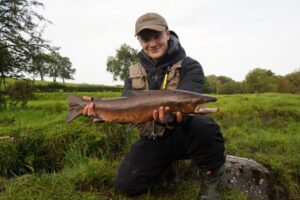 A fly fisherman holds up a large atlantic salmon. 