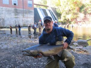 A man holds up a large chinook salmon caught from a dam. 