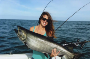 Angler holds up an enormous salmon from a boat. 