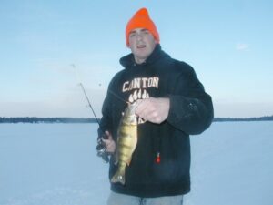 A young man holds up a large yellow perch. 
