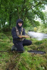A fisherman holds out a brown trout caught on a float setup. 
