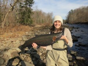 Happy fisherman holds up a large steelhead she caught from the shore. 