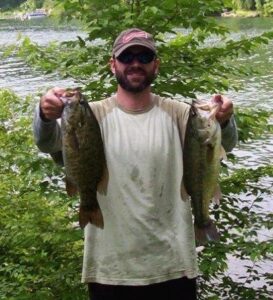 A fisherman holds up two largemouth bass he caught while shore fishing. 