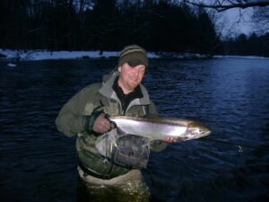 Fisherman holds up an average-sized steelhead caught on a float while river fishing. 