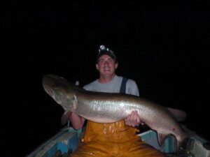 A happy angler holds up a colossal musky while boat fishing. 